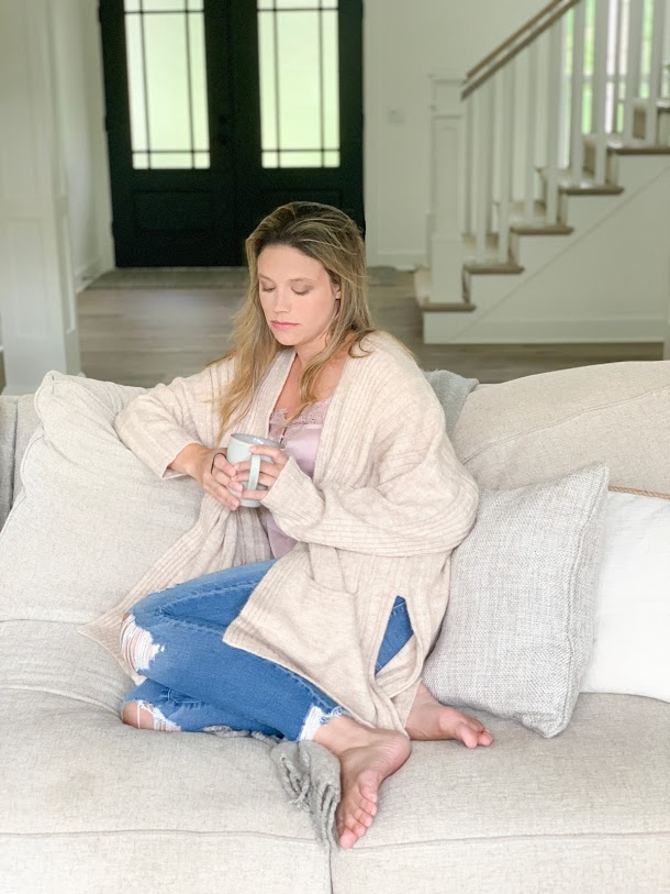 woman in sweater drinking coffee on couch 