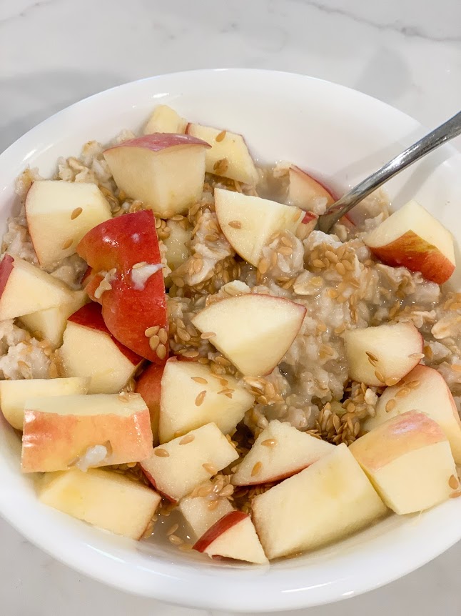 hot oatmeal with apples and flaxseed in bowl with spoon